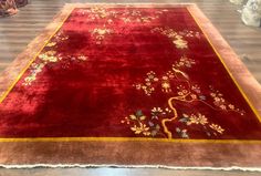 a red rug with flowers and birds on it in the middle of a wooden floor