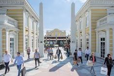 many people are walking around in front of large buildings with columns on the sides and pillars above them