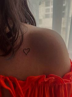 the back of a woman's shoulder with a small heart tattoo on her left shoulder