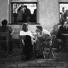 black and white photograph of people sitting at tables in front of a building with open windows