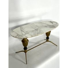 a marble top coffee table with two brass legs and an oval shaped center piece on one end