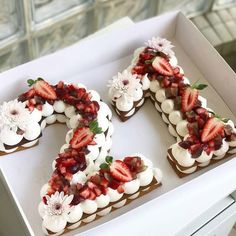 a number shaped cake with strawberries and flowers on it in a white cardboard box