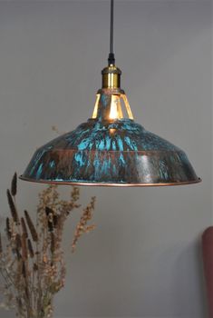 a blue and gold colored light hanging from a ceiling fixture with dried flowers in the foreground