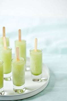 several glasses filled with green liquid and toothpicks sitting on a white platter