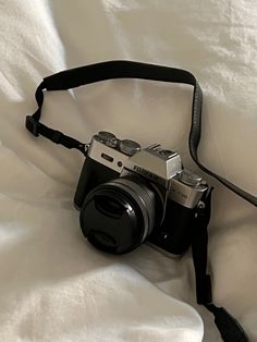 a black camera sitting on top of a white bed next to a strap that is attached to it