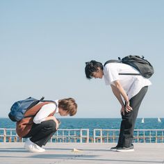 two young men with backpacks on their backs are looking at something in front of the ocean