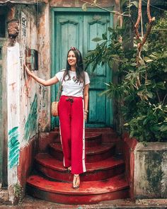 a woman standing in front of a door with her arms out and wearing red pants