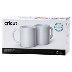 two white coffee mugs sitting next to each other in front of a boxed box