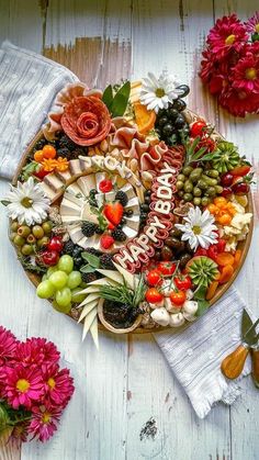 a platter filled with fruit and vegetables on top of a table next to flowers