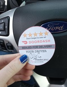 a person holding up a sticker in their hand next to a car steering wheel