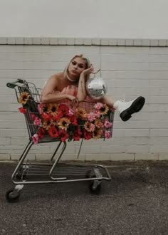 a woman sitting in a shopping cart with flowers on the front and legs, holding a soccer ball