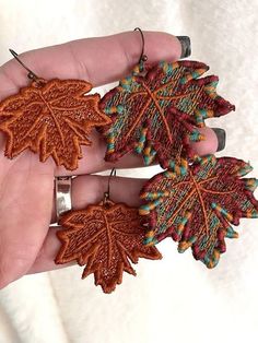 two handmade leaf earrings are shown in the palm of a person's hand