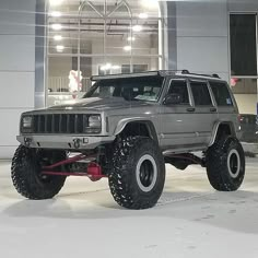 a grey jeep parked in front of a building with snow on the ground and lights above it