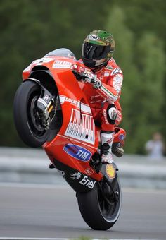 a man riding on the back of a red motorcycle down a race track with trees in the background