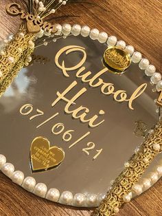 a heart shaped plaque with gold lettering and pearls