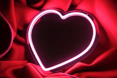 a heart shaped neon sign sitting on top of a red cloth