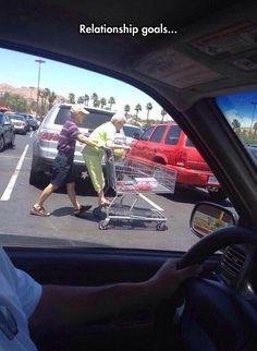 a man pushing a shopping cart through a parking lot with another person in the car