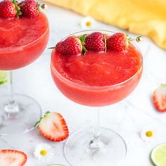 two margaritas with strawberries and lime garnish sit on a marble table