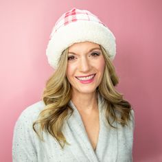 a woman wearing a white and red plaid hat smiles at the camera while standing in front of a pink background