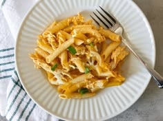 a white plate topped with pasta covered in sauce and green onions next to a fork