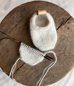 a pair of white knitted slippers sitting on top of a wooden table next to knitting needles