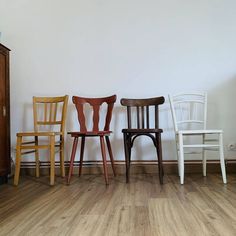 three wooden chairs sitting next to each other on a hard wood floor in front of a white wall