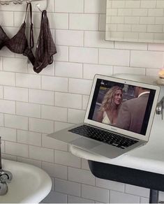 an open laptop computer sitting on top of a white sink next to a bath tub