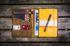 a wallet with a pen, notepad and other items in it sitting on a wooden table