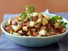 a blue bowl filled with potatoes and bacon on top of a table next to a napkin