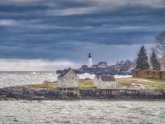 an island with houses and a lighthouse in the distance on a cloudy day near water