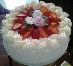 a cake with white frosting and fresh strawberries on top, sitting on a table