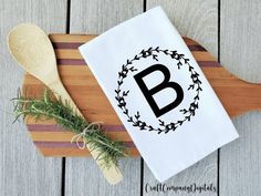 a monogrammed dish towel on a cutting board with a wooden spoon and sprig of rosemary