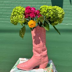 a pink boot with flowers in it sitting on top of a table next to a green wall