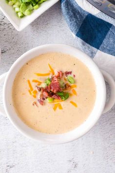 a bowl of potato soup with bacon and green onions on the side next to a plate of broccoli