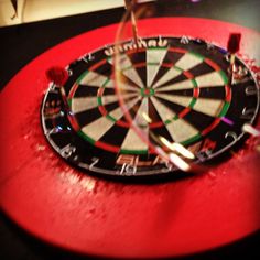 a dart hitting in the center of a bulls eye on a red table with other darts