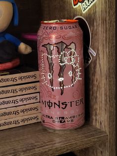 a pink monster energy drink sitting on top of a wooden shelf next to a stuffed animal