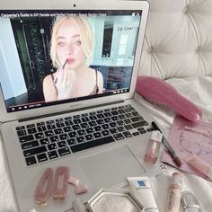 an open laptop computer sitting on top of a bed next to makeup and other items