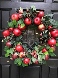 a wreath with apples and leaves is hanging on the side of a black front door