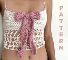 a woman wearing a crochet top with a pink tie around her waist