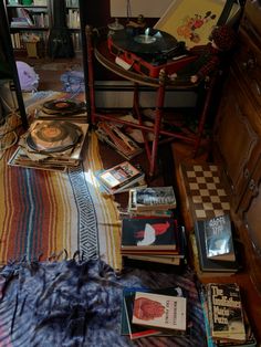 there are many books on the floor next to a record player and a table with a lamp