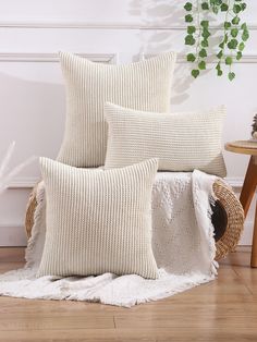 three white pillows sitting on top of a wooden floor next to a basket filled with plants