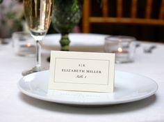 there is a place card on the plate at the table with wine glasses in the background