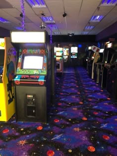 several arcade machines lined up on the floor in a room with blue carpet and purple lighting