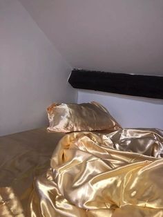 an unmade bed with gold sheets and pillows