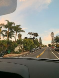 the view from inside a car driving down a street with palm trees and houses in the background