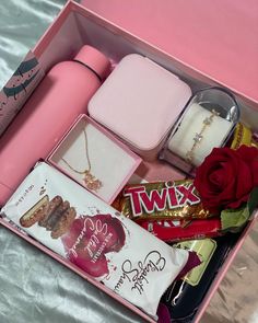 an open pink box with various items in it and a rose on the table next to it