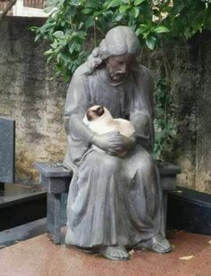 a statue holding a cat sitting on top of a bench