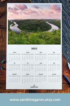 a calendar sitting on top of a wooden table next to a pen and pencils