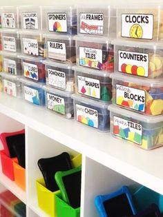 plastic bins filled with different colored items on top of a white shelf in a classroom