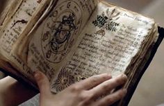 a person holding an open book in their hands with writing on the pages and symbols